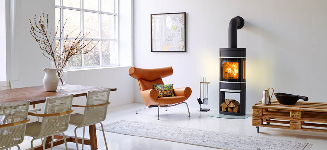 Schwarzer ovaler Holzofen Scan 68 in einem weißen Raum mit einem Designerstuhl in hellem Leder und einem groben Palettentisch mit Rollen