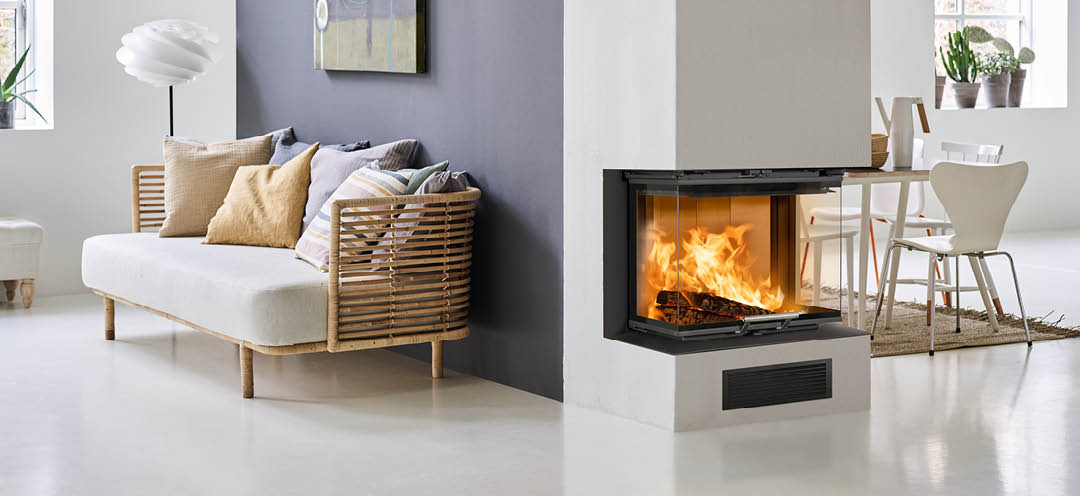 Weißes Wohnzimmer mit Bambussofa und lila Wand mit Kamin an der Stirnwand und Kamineinsatz Scan 5004 FRL mit Glas an drei Seiten