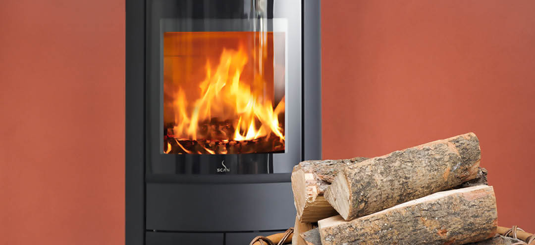 Schwarzer ovaler Kaminofen Scan 68-13 im roten Raum mit großem Holzkorb davor