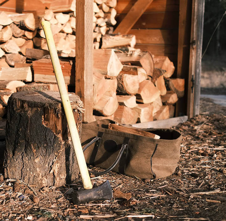 Axt lehnt an einem Hackklotz bei einem offenen Holzschuppen