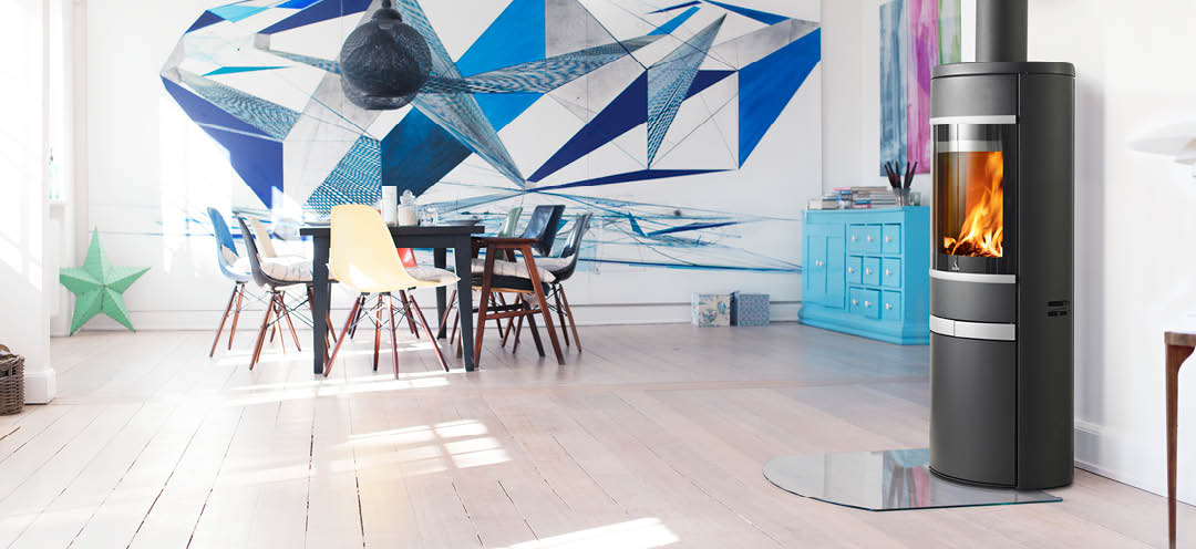 Schwarzer ovaler Kaminofen mit Seitenglas, Aluminiumgriff und Zierleisten Scan 68-12 in einem weißen Wohnzimmer mit großer Grafik über dem Esszimmer