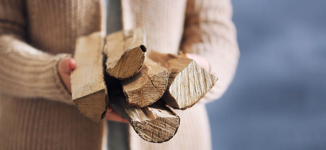 Frau mit beiger Strickjacke hält Brennholz in ihren Händen