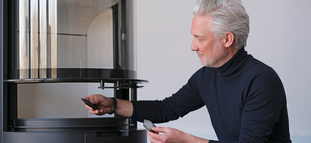 Mann mittleren Alters im hochgeschlossenen Pullover Designer Niels Kjeldsen zeigt Glasgriffe vor Kamin Scan 87