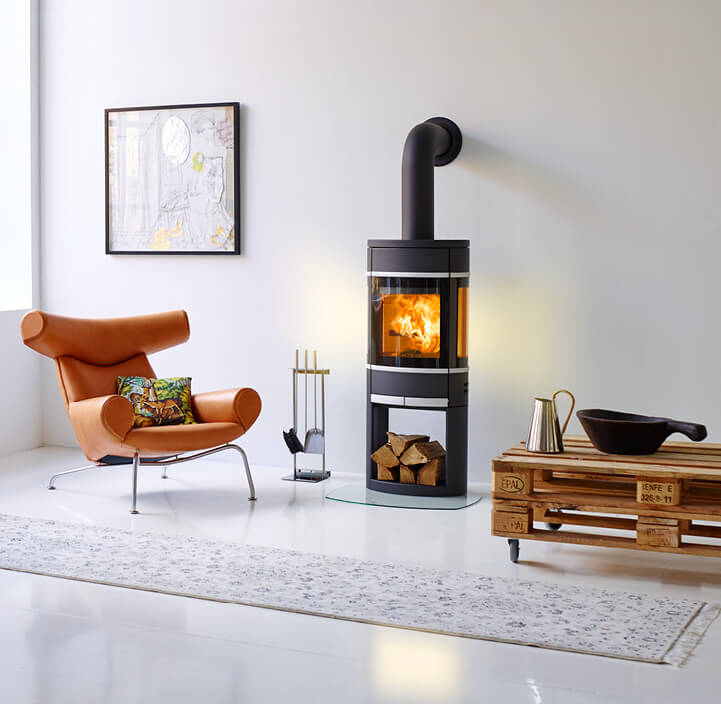 Schwarzer Kamin Scan 68 brennt in einem weißen Raum mit einem cognacfarbenen Stuhl und einem Palettentisch daneben