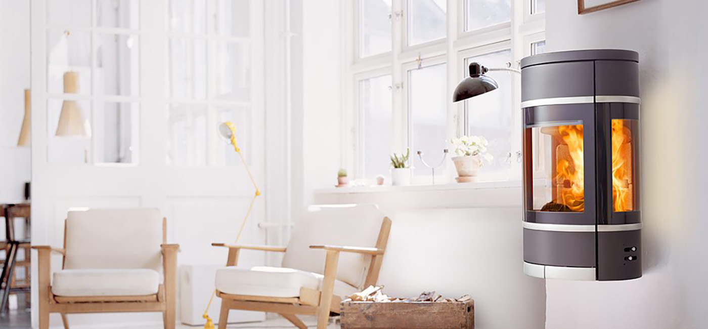 Schwarzer ovaler wandhängender Kaminofen mit seitlichem Glasgriff aus Aluminium und Zierleisten Scan 68-8 in einem weißen Raum mit hellen Möbeln im dänischen Designstil