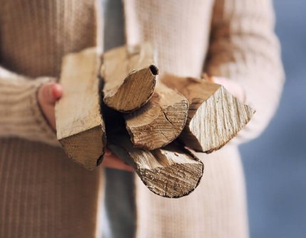 Frau in beiger Strickjacke, die Holz in ihren Händen trägt