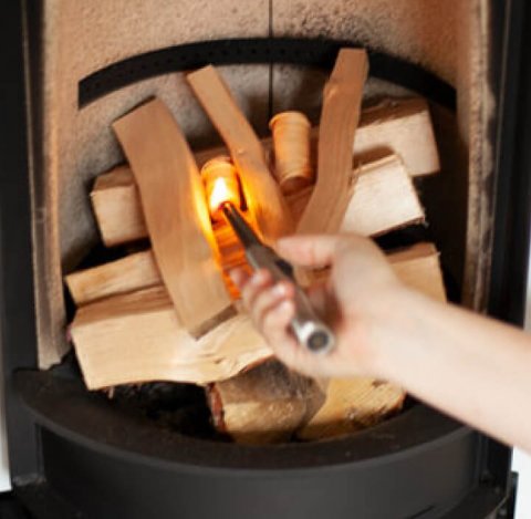 Stapelfeuer in einem Scan 83-2-Holzofen und eine Frauenhand, die es anzündet